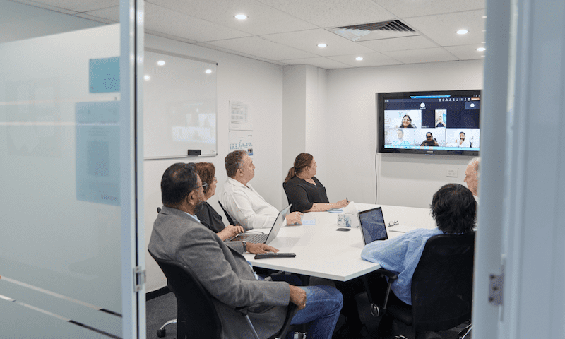 The team at Fortuna Advisory Group meet in a board room-style setting. There are some team members dialling into the call, with their faces showing on the video call screen.