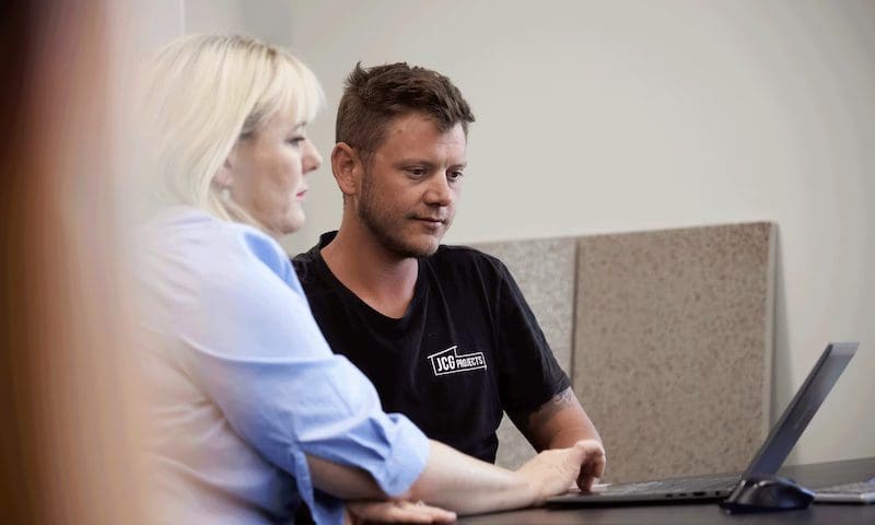 Johnno, a small business owner, sits at a laptop with his accountant Olivia discussing the numbers.