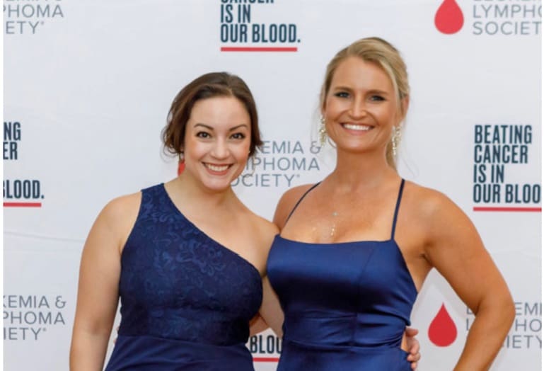 Two women in formal wear stand together in front of a Lowcountry Leukemia & Lymphoma Society banner