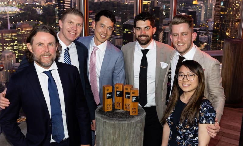 A group of Xero Award winners gather around their trophies against a skyline backdrop of Melbourne city.